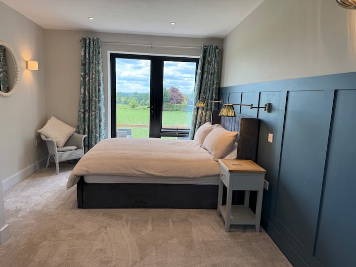 Dormitorio principal con vista a las colinas de Shropshire. Cama doble, mesas auxiliares, silla y acogedoras luces de pared
