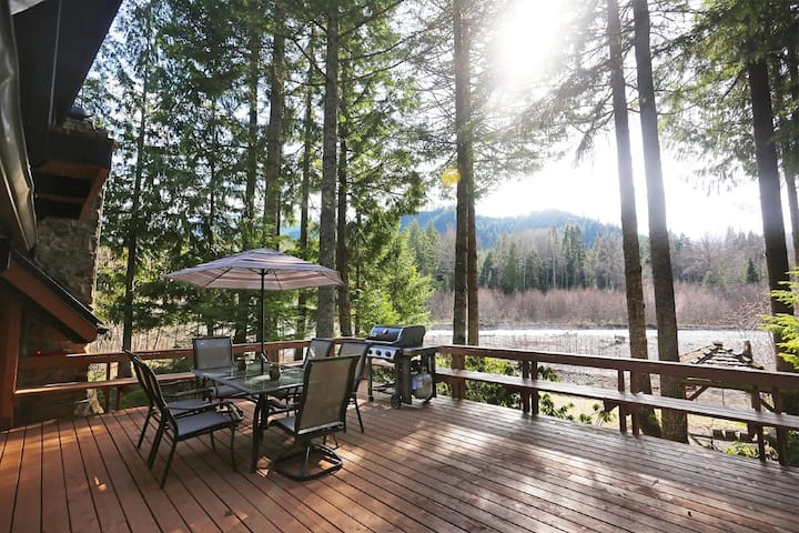 Back deck with a table, umbrella and grill, looking across the river to a forested ridge