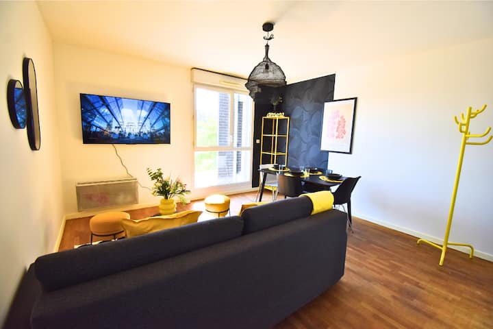 Acogedor salón con televisión montada en la pared, decoración cuidada y elegante zona de comedor. Ambiente moderno y luminoso, ideal para relajarse o compartir un momento agradable después de un día en París.