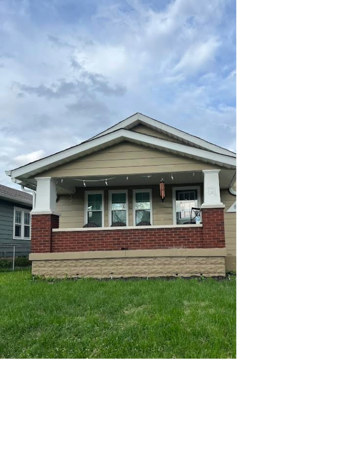 The exterior of a bungalow features a welcoming front porch with multiple windows and a combination of beige and red brick siding. A green lawn surrounds the home, complemented by a cloudy sky overhead.