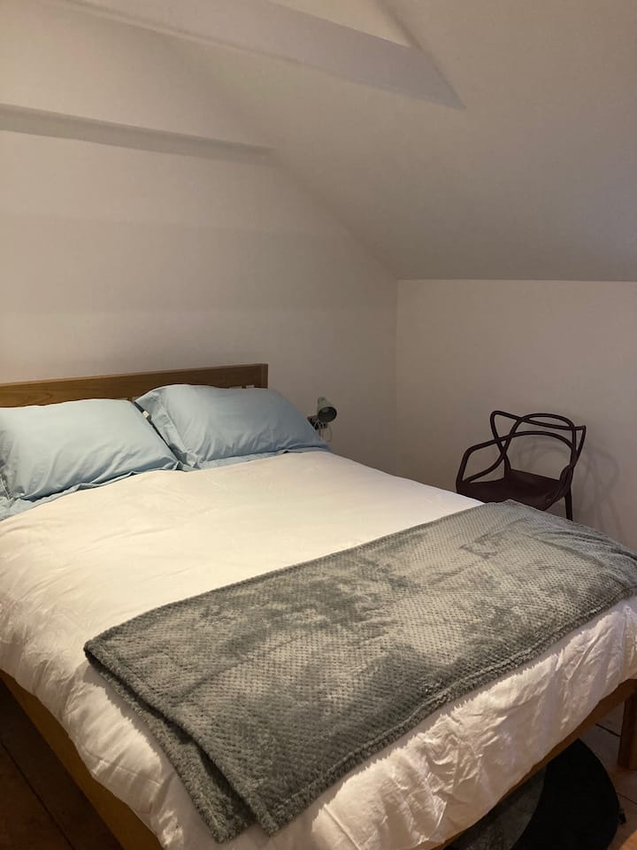 Main bedroom at Little Beside Cottage with a comfortable queen-size bed, soft linens, and views over the sunny front garden — a peaceful retreat after a day exploring Cornwall’s coast.