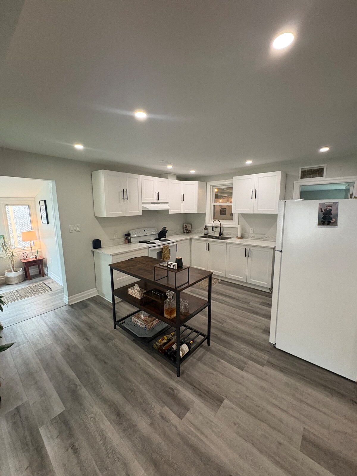 A thoughtfully arranged kitchen features white cabinetry and modern appliances. A central island offers additional prep space and is styled with decorative items. Natural light enters through a nearby window, illuminating the open layout, which connects to an inviting dining area.