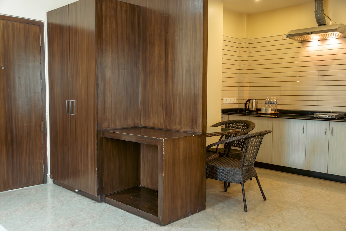 The image displays a compact kitchenette area featuring a sleek countertop and built-in cabinetry. A small seating nook with a rustic table and a chair is visible, complementing the functional design of the space.