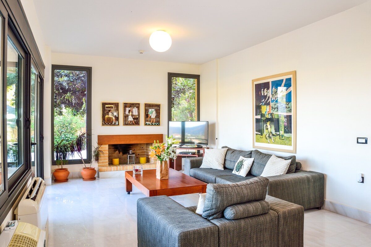 الطابق الأرضي: غرفة معيشة واسعة مع تلفزيون وسريرين أريكة وأبواب زجاجية كبيرة تفتح على سطح حمام السباحة