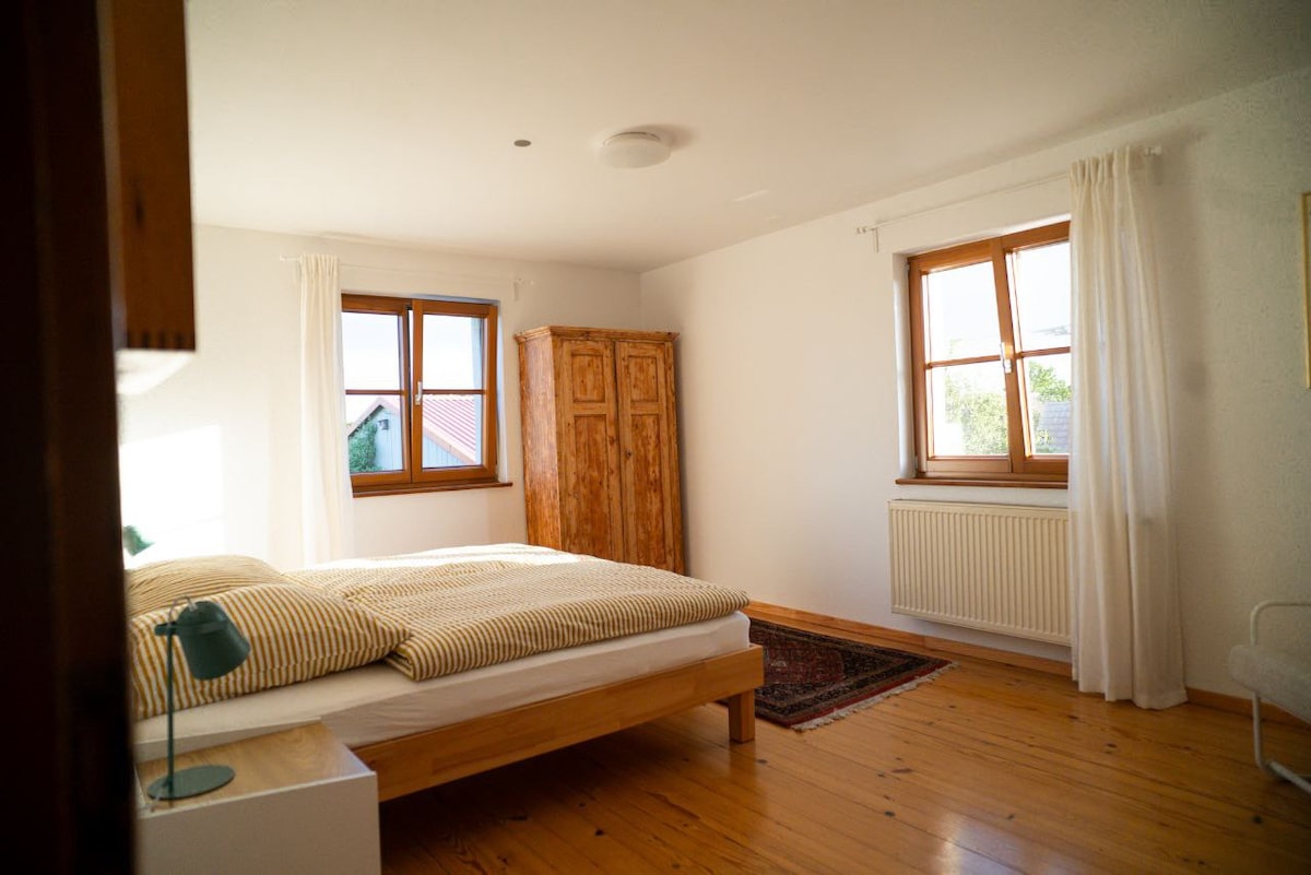 Im lichtdurchfluteten Schlafzimmer sorgen ein komfortables Doppelbett, ein Sessel zum Zurücklehnen sowie Schrank und Garderobe für Ordnung und Gemütlichkeit. Für erholsamen Schlaf lässt sich der Raum durch Fensterläden komplett abdunkeln.