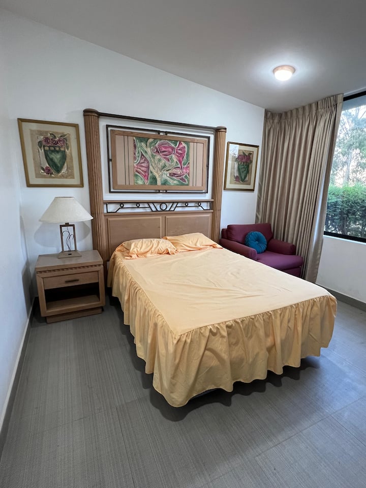 Dormitorio secundario amplio y privado con cama de gran formato y ventanales panorámicos que ofrecen vistas al jardín. Un refugio de paz diseñado con detalles de madera y luz natural para garantizar un descanso reparador.
