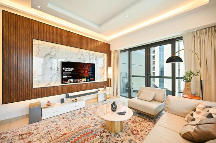 ห้องนั่งเล่นที่กว้างขวางและมีสไตล์พร้อมผนังสื่อหินอ่อนหรูหราโซฟารูปตัว L หรูหราและสมาร์ททีวี หน้าต่างสูงจากพื้นจรดเพดานเปิดออกสู่ระเบียงทำให้ที่พักเต็มไปด้วยแสงธรรมชาติ เหมาะสำหรับการพักผ่อนหรือความบันเทิง