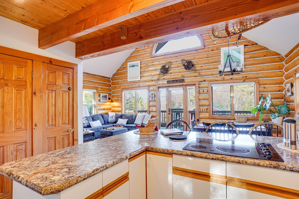 The spacious kitchen area features a peninsula counter with bar seating for three. Light-colored cabinetry complements the granite countertop. Above, a vaulted ceiling with wooden beams enhances the open atmosphere, while large windows allow natural light to illuminate the cozy living space.