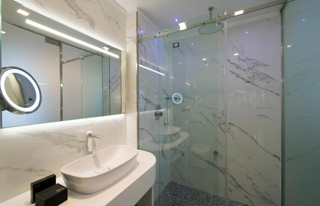 A modern bathroom features marble walls and a walk-in shower with glass doors. A round mirror and a sleek sink are positioned over a minimalist countertop. Soft lighting illuminates the space, creating a clean and open atmosphere.