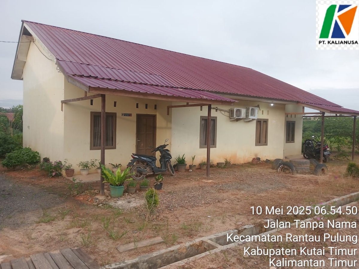 A simple one-story building with a red metal roof is situated on a predominantly gravel lot. Two air conditioning units are mounted on the exterior walls, and parked motorcycles are visible in front of the entrance. A calm, rural setting surrounds the property.