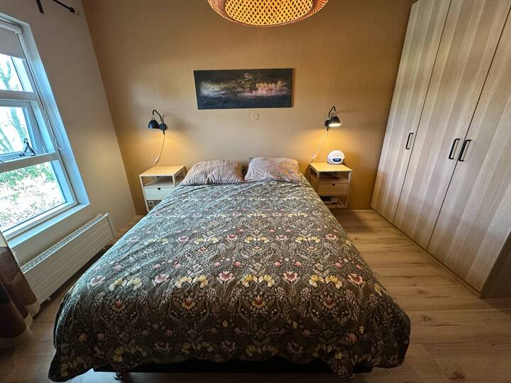 Cama tamaño queen, capacidad para 2 personas, 2 mesitas de noche con enchufes eléctricos debajo de ambas.