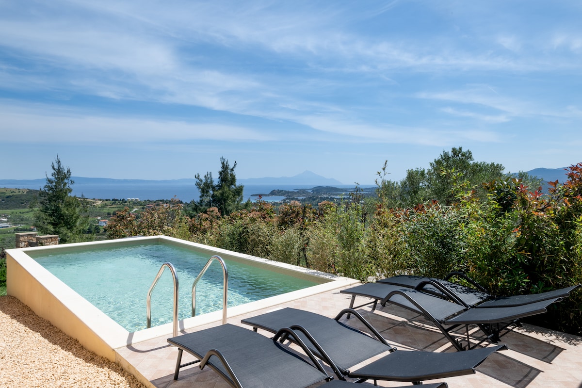 A private swimming pool is surrounded by comfortable sunbeds, offering a relaxing area to take in the stunning views of Diaporos Island and the third peninsula. Lush greenery frames the scene, highlighting the serene outdoor ambiance.