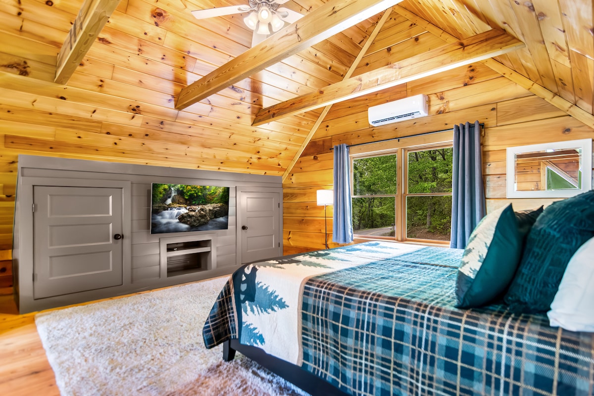 Уште еден поглед кон креветот на поткровјето, прикажувајќи ги големите прозорци со слики кои ја исполнуваат собата со природна светлина и поглед кон бујното зеленило.