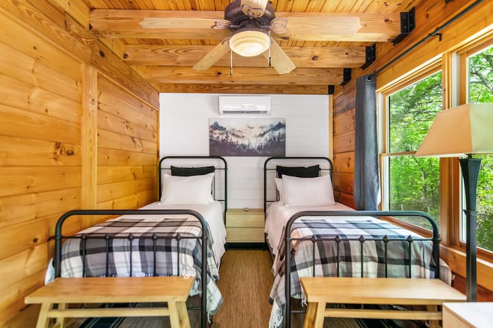 ห้องนอนสว่างสดใสและสดชื่น มีเตียงเดี่ยว 2 เตียง เครื่องนอนผ้าฟลานเนลสีเดียวกัน พัดลมเพดาน และวิวทิวทัศน์ป่าไม้