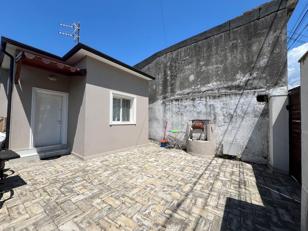 A private outdoor patio is shown, featuring a stone-paved surface surrounded by high walls. A door leads into the property from one side, while a barbecue grill is positioned against the back wall. A table and bench seating area are visible to the left.
