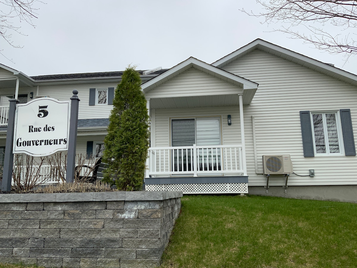 The front entrance is marked by a clearly visible address sign and features a small, covered balcony. A low stone wall borders the well-maintained lawn, while a small air conditioning unit is positioned beside the entrance door.
