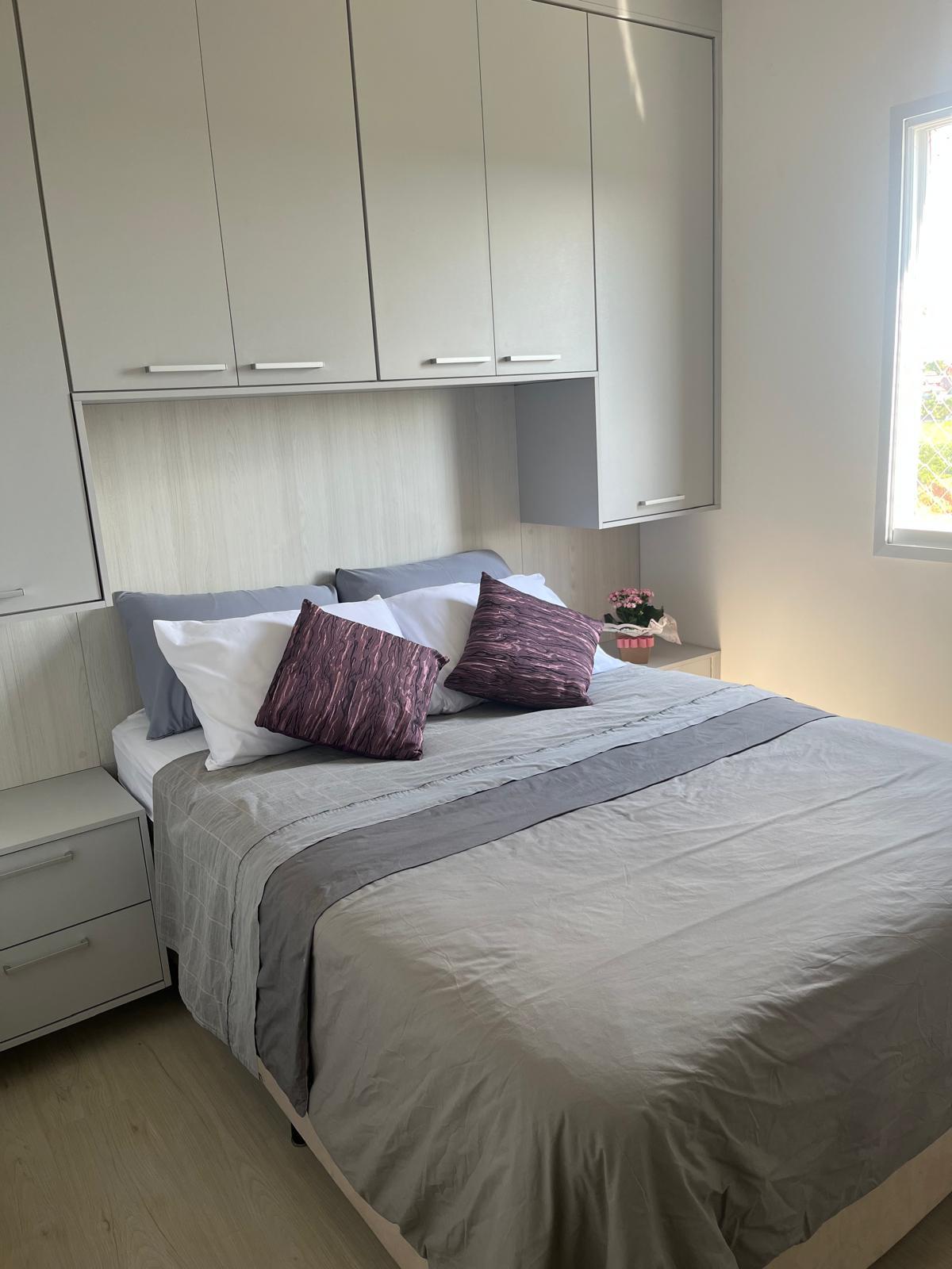 A serene sleeping area features a spacious bed dressed in neutral tones. Decorative pillows add subtle color accents. Built-in cabinets provide ample storage, while a small bedside table holds a potted plant. Natural light is let in through the nearby window.