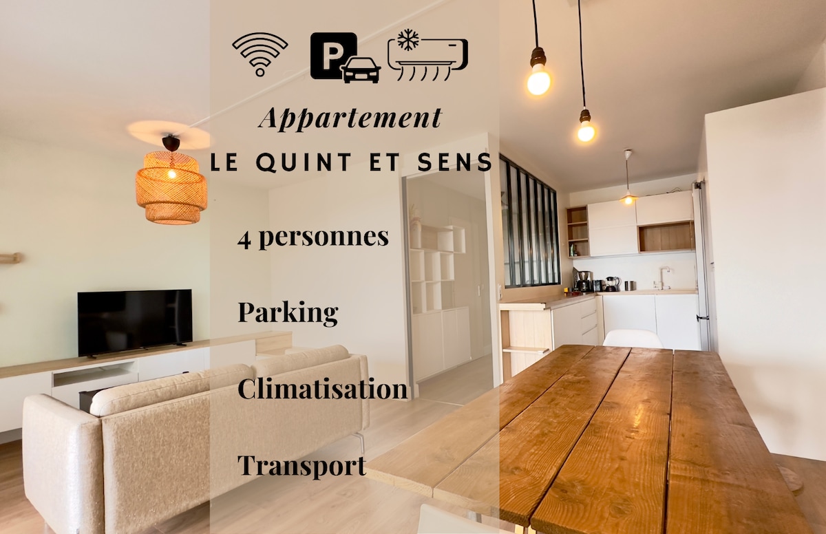 A modern living space is presented, featuring a comfortable beige sofa facing a wall-mounted television. A wooden dining table invites gatherings, while hanging light fixtures provide soft illumination. An open kitchen area is visible in the background, showcasing cabinetry and essential appliances.