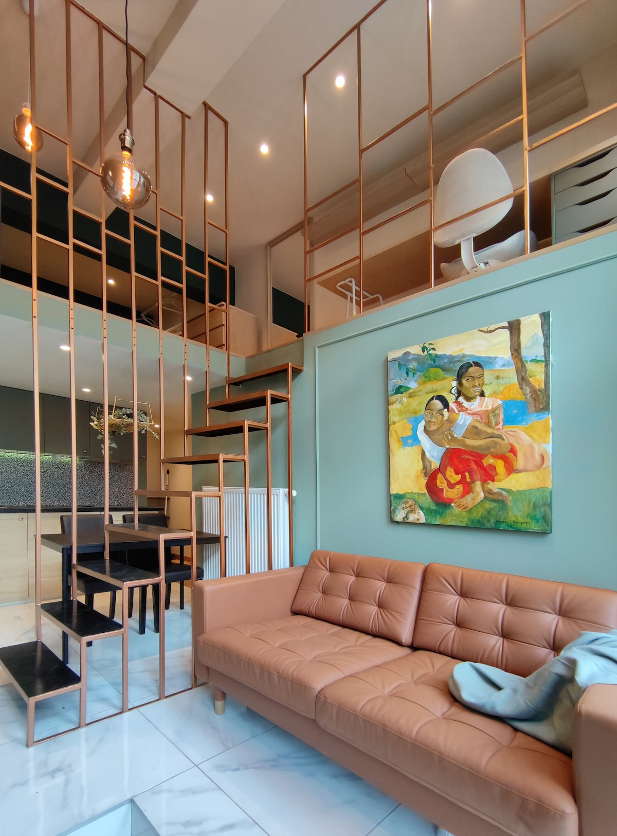 A contemporary living area features a warm-toned sofa paired with a light blue throw. A vibrant painting adorns the wall, depicting two figures in a serene setting. A stylish metal partition adds a modern touch, and a staircase leads to an upper level, while a dining table is visible in the background.
