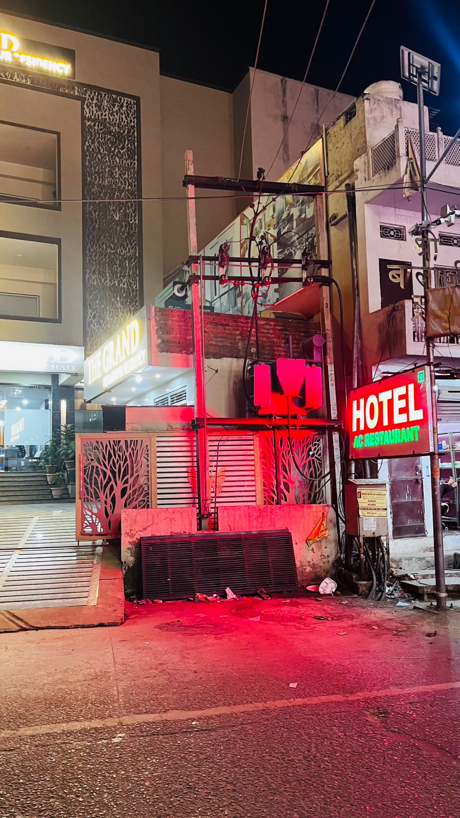 The scene features a street view at night, where neon signs including 'HOTEL' and 'RESTAURANT' illuminate the surroundings. A mix of buildings is present, with one structured around a wide staircase. Bright red lighting creates a vibrant atmosphere along the street.