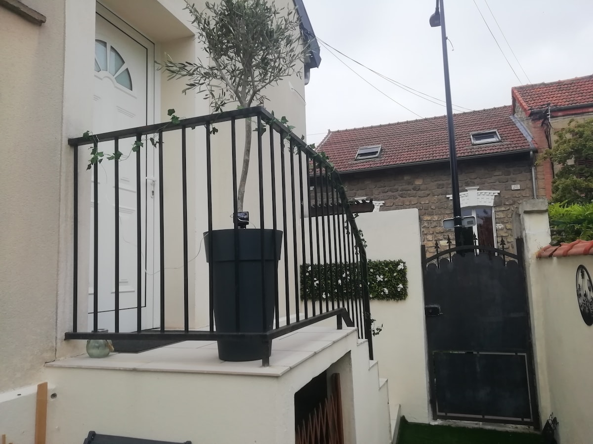 A small terrace is showcased, featuring a railing and a potted olive tree. The area offers a transition from indoors to outdoors. The entrance door is visible, and a gated area can be seen in the background, highlighting the property's exterior.