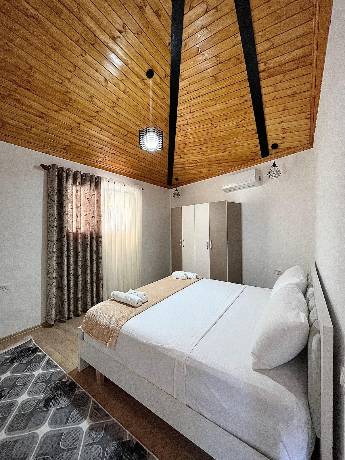 Un dormitorio espacioso con un techo de madera inclinado y una cama nueva y cómoda para una estancia tranquila.




