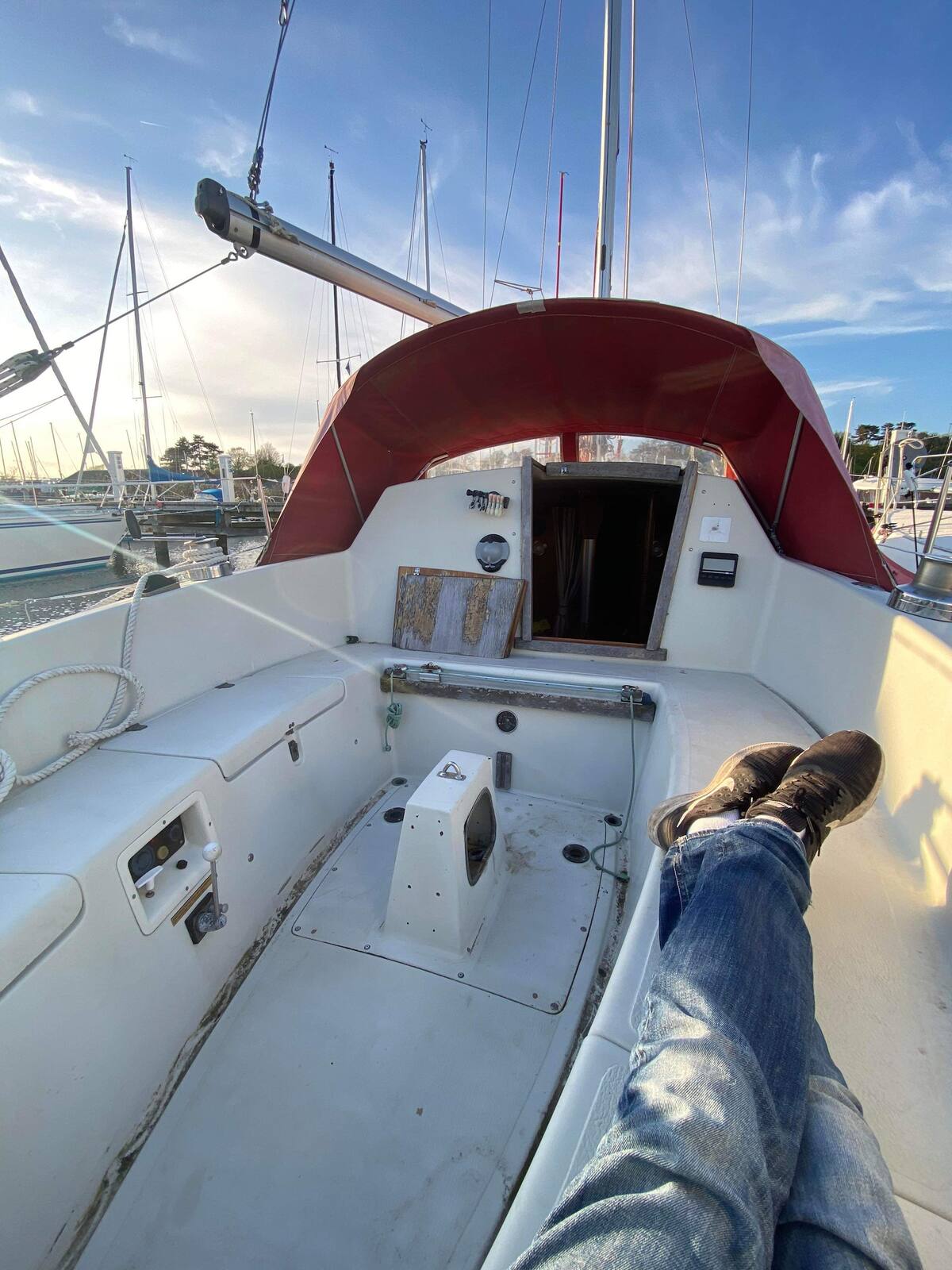 An interior view of the sailboat shows a spacious area, featuring a red canopy overhead. A well-maintained, uncluttered deck allows for relaxation. The helm and access to the cabin are visible, along with ropes and equipment neatly arranged along the sides.