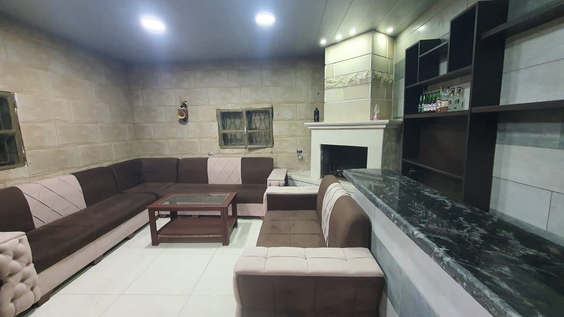 A spacious living area features a large sectional sofa in neutral tones, arranged around a wooden coffee table. A sleek bar with a dark countertop is positioned against one wall, complemented by a soft glow from recessed lighting. The room's stone accent walls add texture.