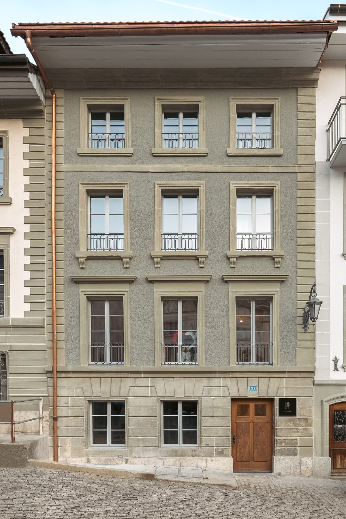 The building's exterior showcases a charming mix of stone and textured plaster, featuring multiple windows with decorative balconies. A solid wooden door serves as the entrance, framed by a traditional lantern. The structure's overall appearance reflects the architectural style of the historical neighborhood.