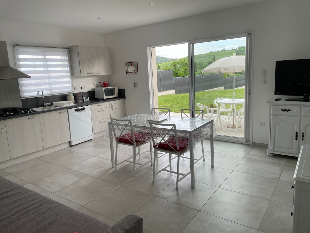 A modern kitchen features light cabinetry and stainless steel appliances, including a gas stove and microwave. A dining table with six chairs is positioned near a large sliding door, allowing natural light to enter and providing views of the outdoor space with a patio umbrella.