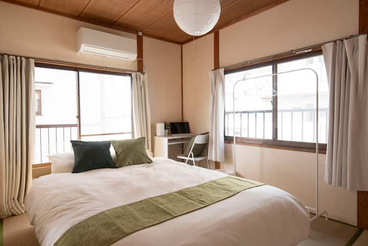 A spacious Japanese-style room with a double bed, work desk, and hanger rack.