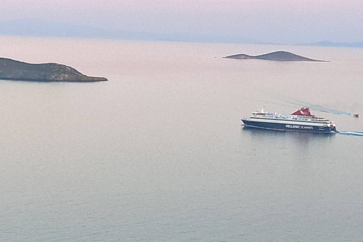 A ferry is seen navigating through calm waters, leaving a gentle trail behind. Scenic islands dot the horizon, set against a soft pastel sky. The tranquil seascape is reflective of the serene surroundings, creating a peaceful atmosphere.