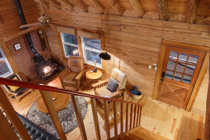 Looking down at the first floor from the top of the stairs. The log home's lower level features a bedroom with a queen bed, full bathroom, kitchen, living room and dining room. 