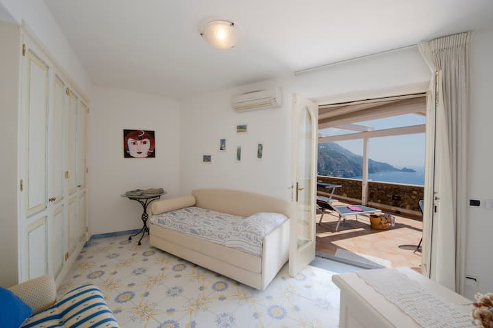 Svetlá a útulná izba s dvoma samostatnými lôžkami, svetlým nábytkom, zdobenou majolikou a priamym prístupom na terasu s výhľadom na more. Relaxačné a funkčné prostredie ideálne pre dospelých alebo deti s dostatkom priestoru a prirodzeným svetlom.