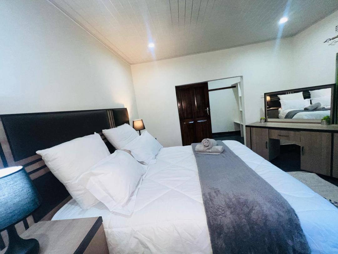 A spacious master bedroom is presented with a large bed, complemented by two bedside lamps. Soft white linens are neatly arranged, and a gray throw is placed at the foot of the bed. A mirrored dresser adds depth to the room, enhancing its welcoming ambiance.