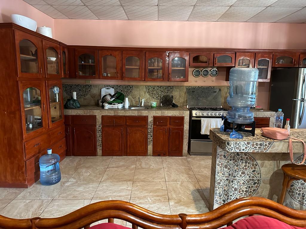 The kitchen features wooden cabinetry with glass-front doors, providing visibility of dishware. A large water dispenser is situated on one side. The countertops are made of stone, complemented by a patterned backsplash. Modern appliances, including a gas stove and refrigerator, are present, contributing to functionality.