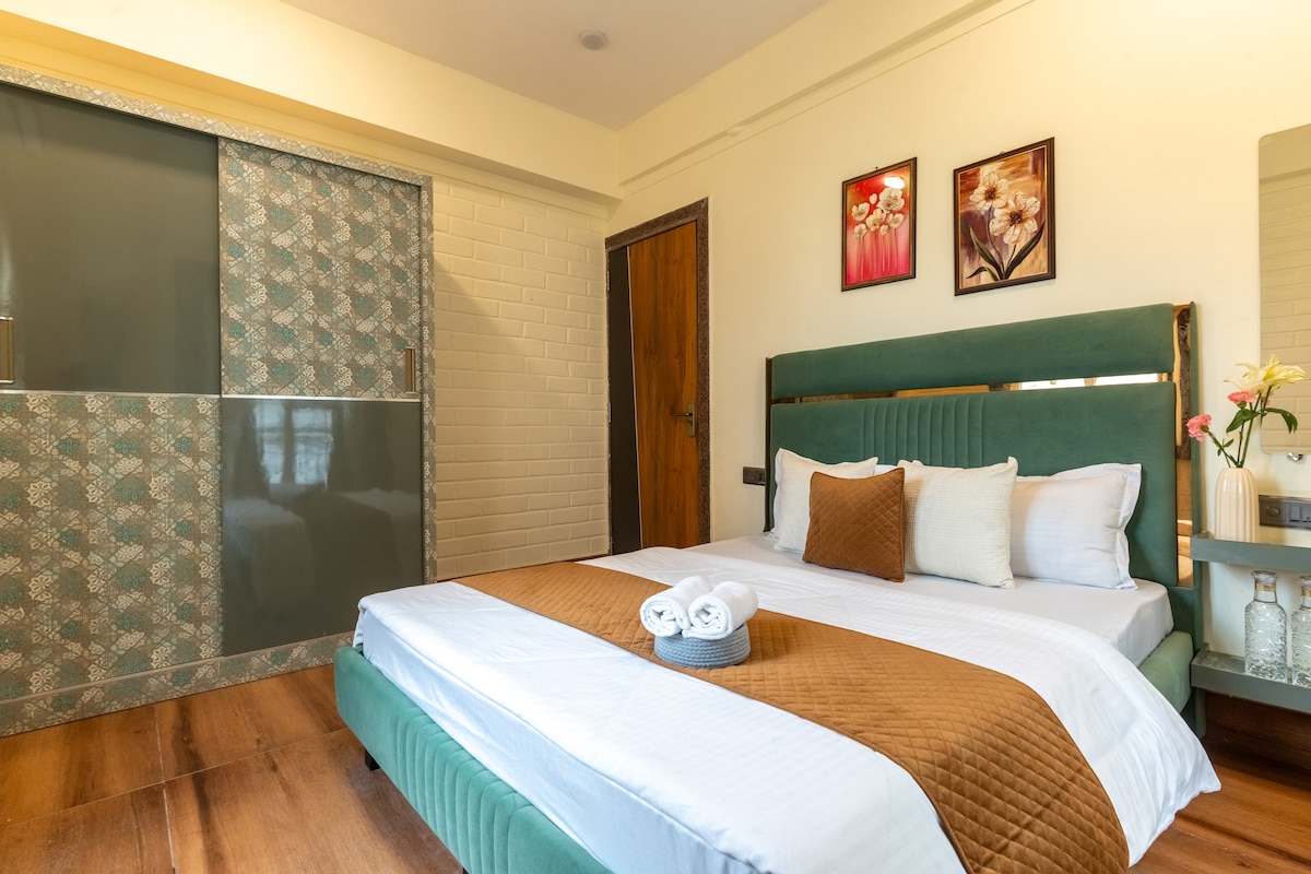 A spacious sleeping area features a comfortable bed adorned with a quilted brown throw. Decorative pillows add a touch of style. Two framed artworks hang above the bed, and a sleek closet is positioned to the left, complementing the room's modern design.
