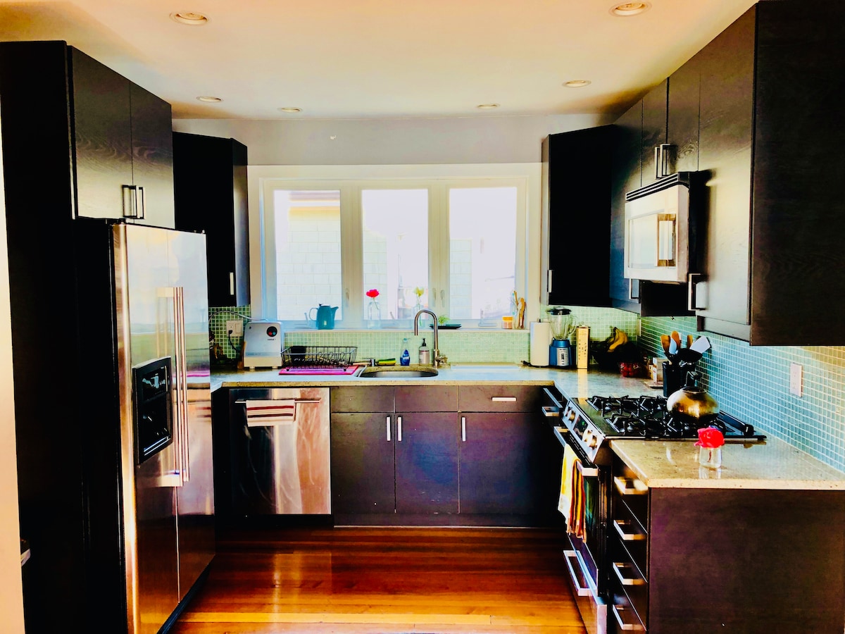 The kitchen features modern cabinetry with stainless steel appliances, including a refrigerator and gas range. A window allows natural light to fill the space, highlighting the granite countertops and colorful backsplash. Ample storage and workspace are provided, making it suitable for cooking and meal preparation.