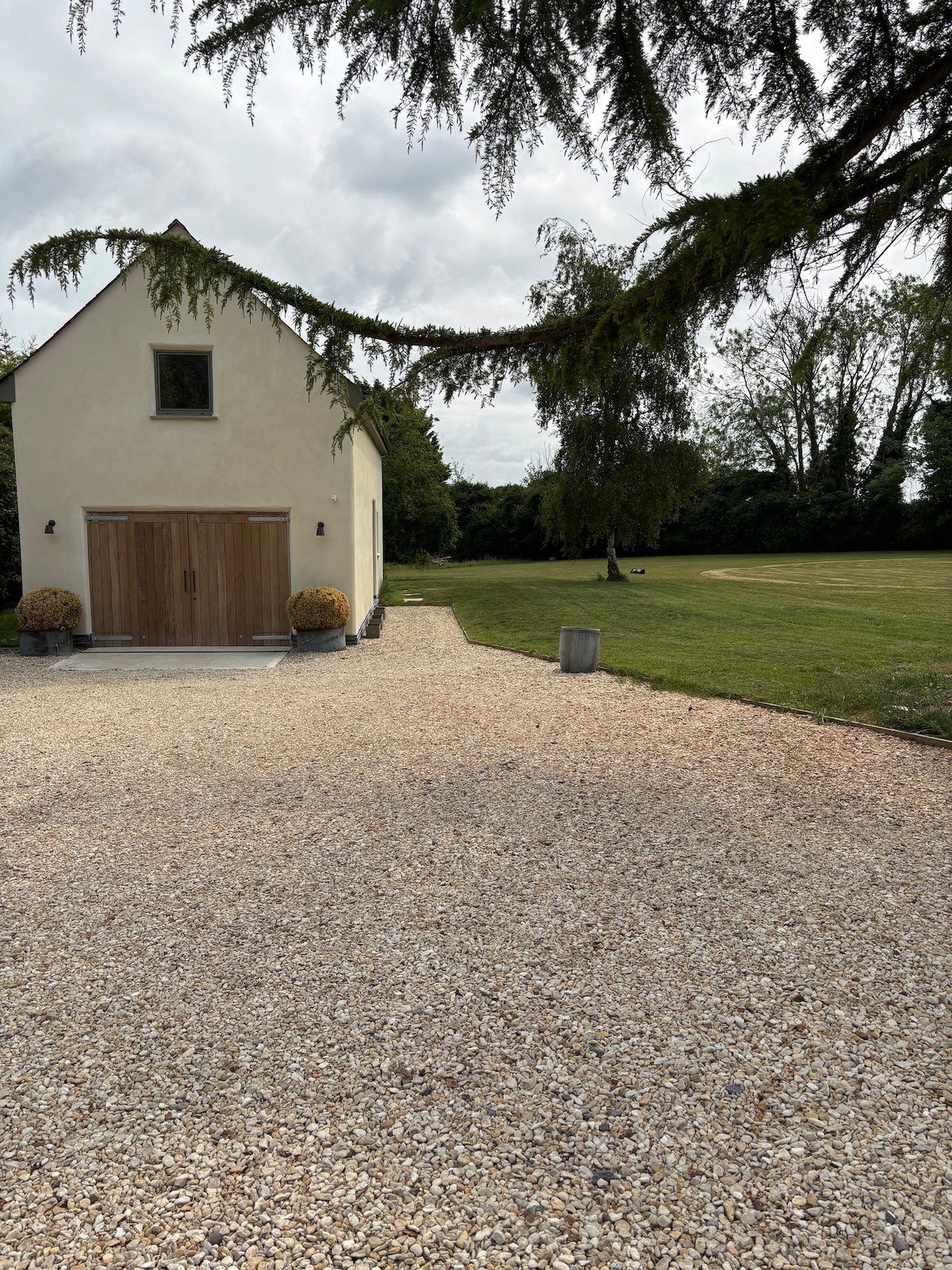 A gravel pathway leads to the charming entrance of the coach house. Lush greenery surrounds the area, providing a sense of tranquility. Decorative plants are positioned near the door, while an expansive lawn extends beyond, offering a peaceful outdoor space.