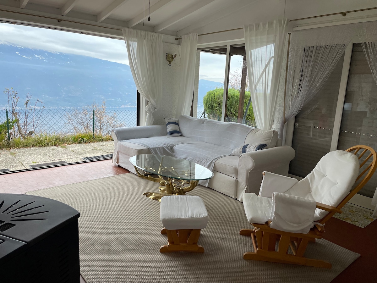 A bright living area is equipped with a spacious white sofa and a glass coffee table. Large windows offer expansive views of the surrounding landscape. Soft curtains frame the windows, while a rocking chair provides additional seating in this relaxed space.