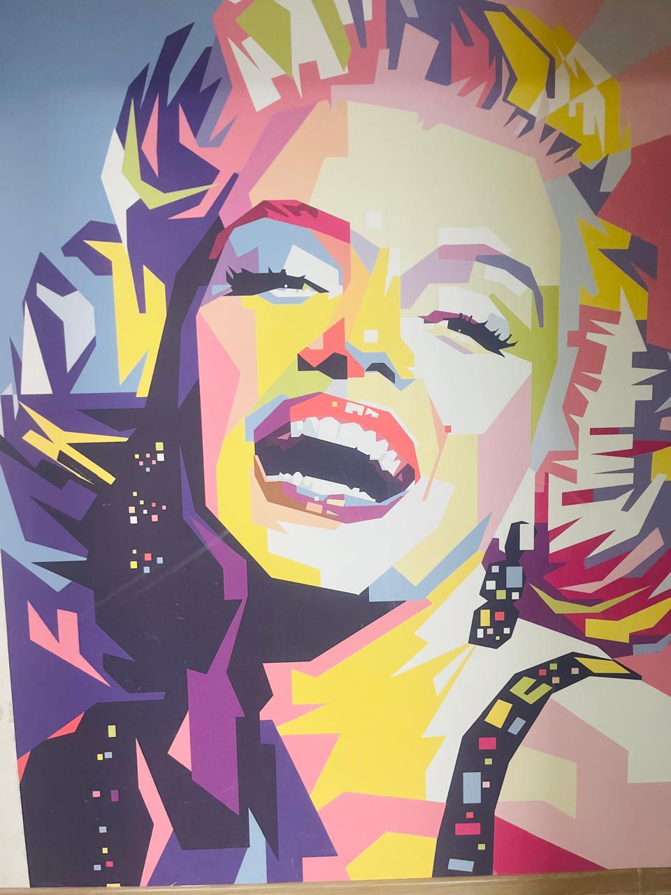 A vibrant mural takes center stage, featuring bold colors and abstract shapes. The artwork incorporates deep blues, bright yellows, and striking purples, creating a dynamic visual impact. The surrounding area is well-lit, enhancing the mural's lively design and adding a unique touch to the space.