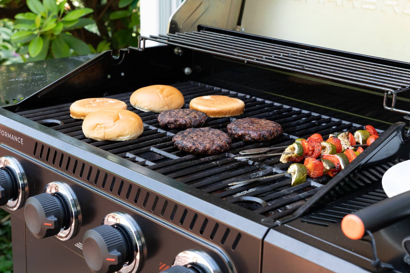 Grill with burgers, veggies, and skewers cooking