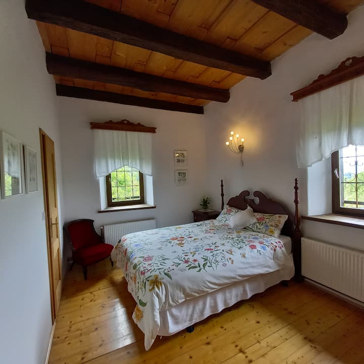 Bedroom 1: Private Room with Garden and Hill Views. Unwind in this space with a private bathroom and enjoy stunning views of our lush rose garden and the rolling green hills beyond. The natural wood accents add to the tranquil  atmosphere.