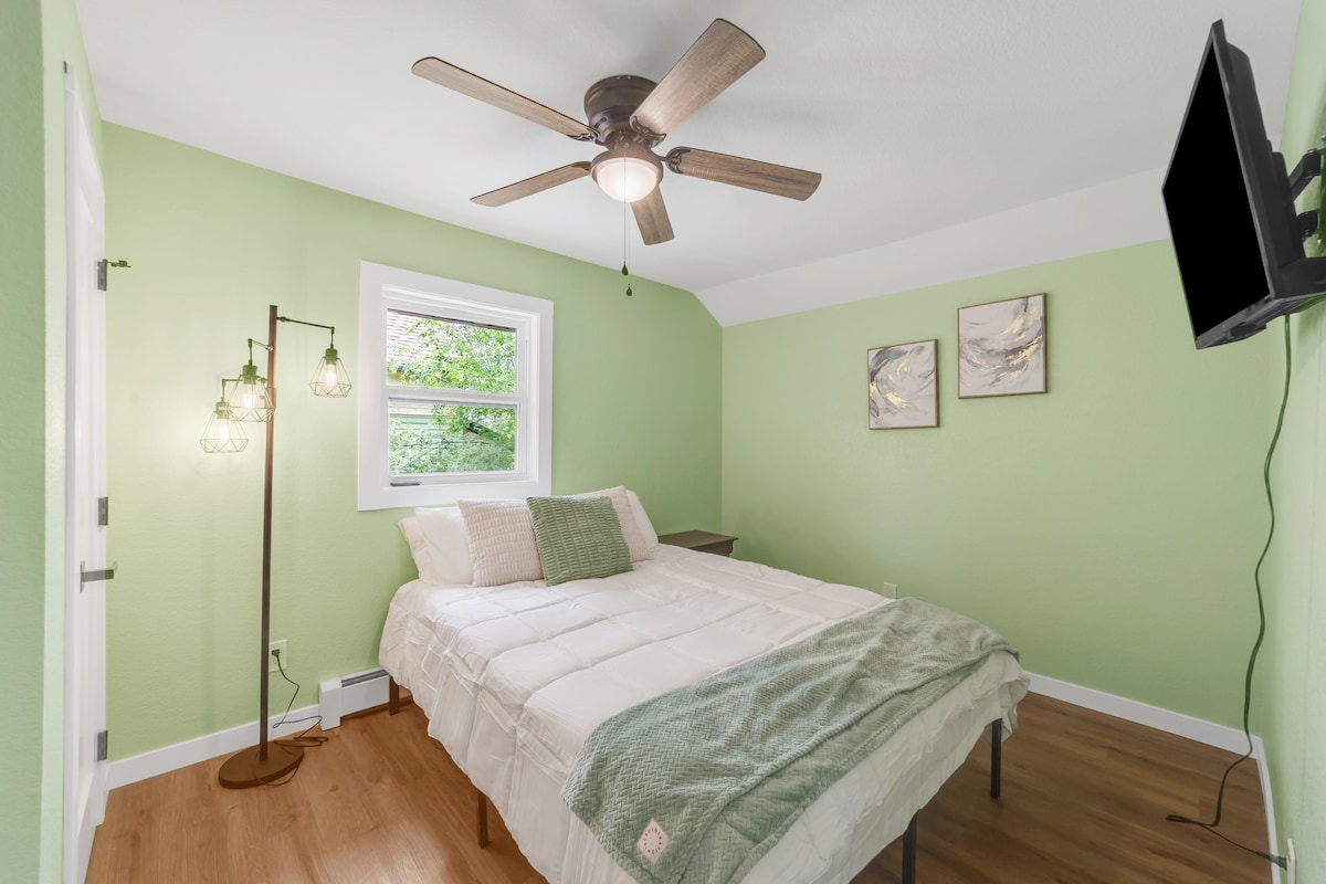 Táto útulná spálňa je zariadená v jemnej zelenej palete a má pohodlnú posteľ s vrstvenými vankúšmi a ľahkou prikrývkou. Užite si namontovanú televíziu, stropný ventilátor a teplé prirodzené svetlo, ktoré priestor napĺňa a prispieva k relaxačnému pobytu.