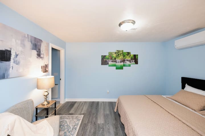 Amplio dormitorio con cama tamaño king con decoración moderna, sillón, iluminación suave y ambiente tranquilo, ideal para parejas o huéspedes individuales.