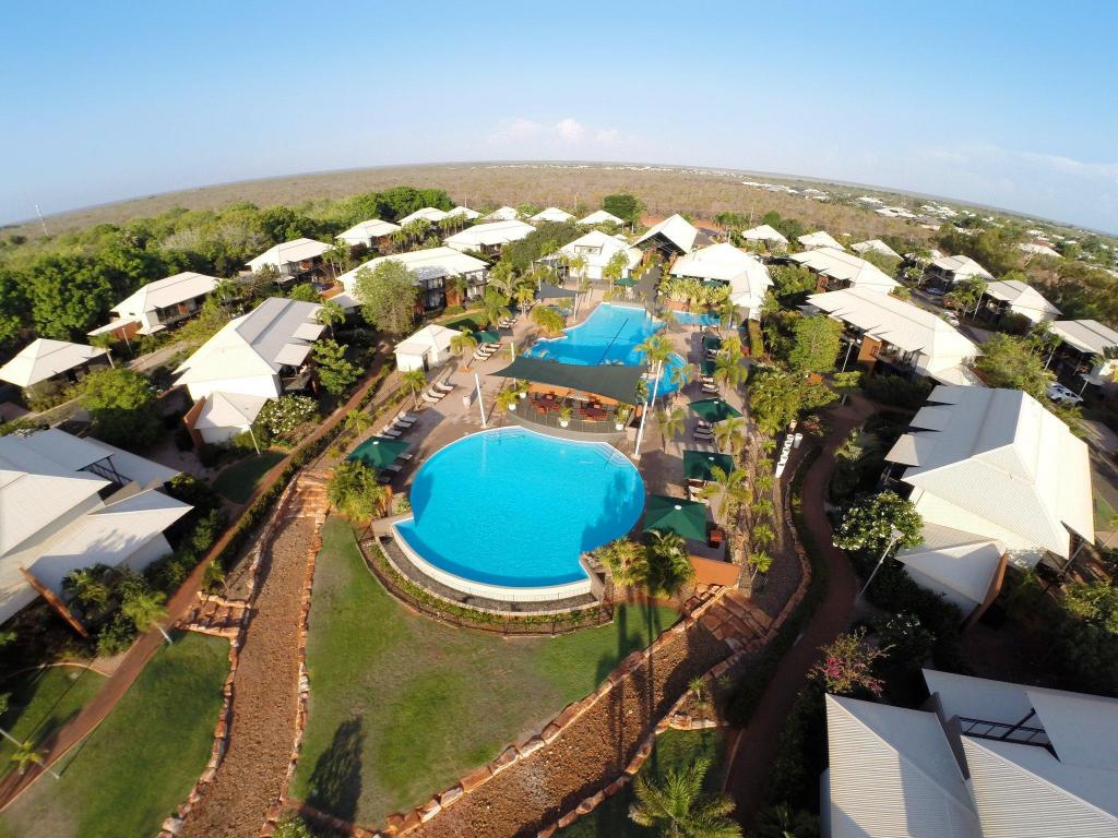 An aerial view showcases the resort complex with five swimming pools surrounded by lush greenery. The infinity pool and large resort pool are prominently displayed in the center, while various lounge chairs and vibrant landscaping are visible throughout the property.