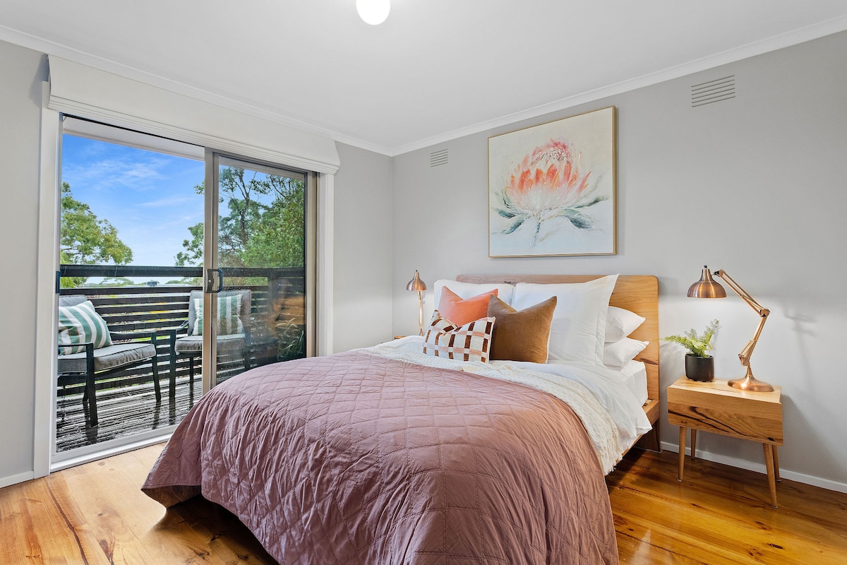 Გააღვიძეთ ხეების ხედი ძირითად საძინებელში, რომელიც მოპირკეთებულია ორადგილიანი საწოლით, აივანზე გასასვლელით და სპილენძის საწოლისპირა ლამპებით.