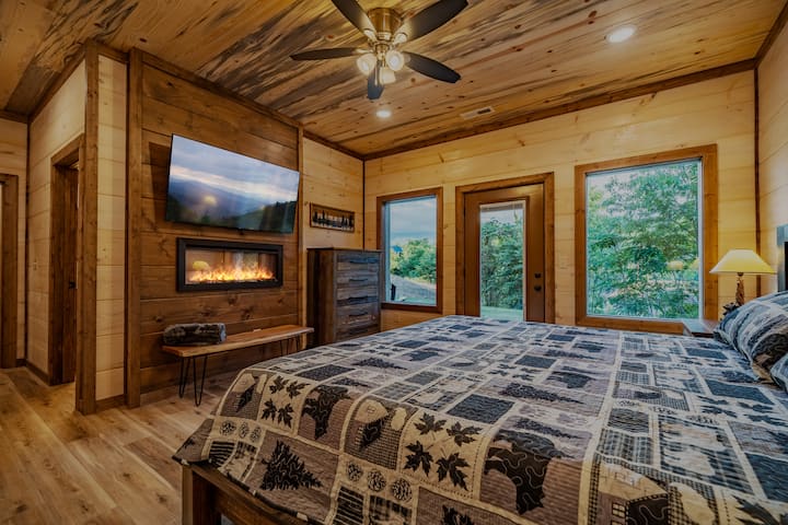 חדר שינה קינג-סייז בקומה התחתונה עם חדר רחצה צמוד, קמין חשמלי פנימי וטלוויזיה חכמה 55 אינץ'.