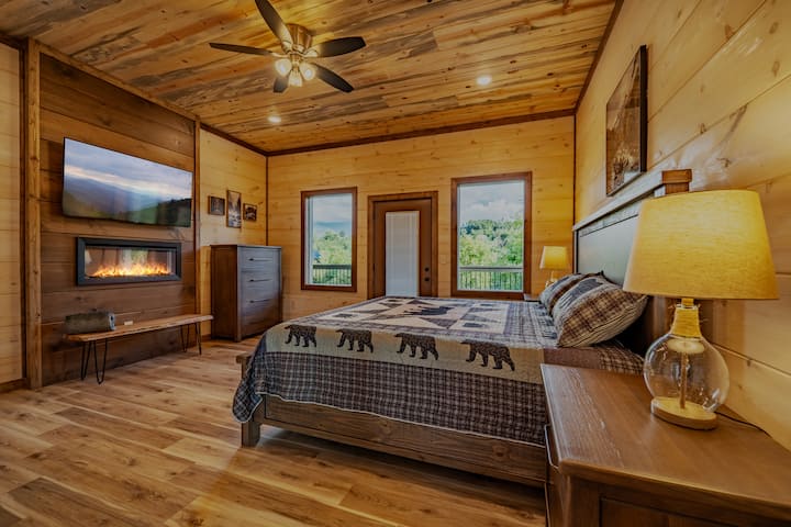 חדר שינה ראשי בגודל קינג סייז בקומה הראשית עם חדר רחצה צמוד, קמין חשמלי פנימי וטלוויזיה חכמה 55 אינץ'.