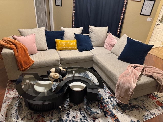 A spacious sectional sofa sits in a welcoming living area, adorned with decorative pillows in pink and navy. A cozy throw blanket rests casually on the armrest. In front, a unique coffee table features a circular design and decorative items, all placed atop an area rug with a vibrant pattern.